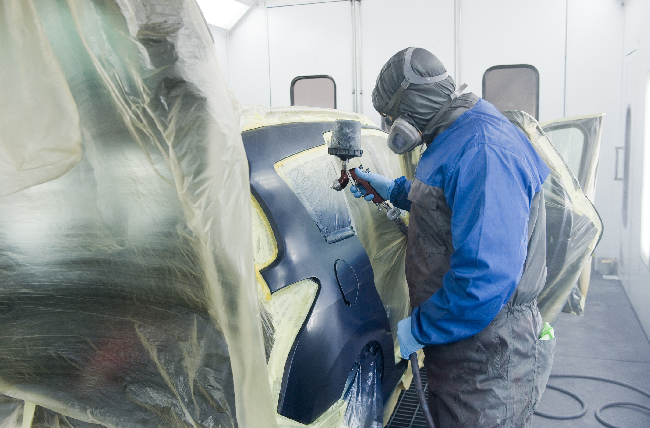 A professional car painter who is painting the body work of a car in a paint box of a garage with an airbrush.